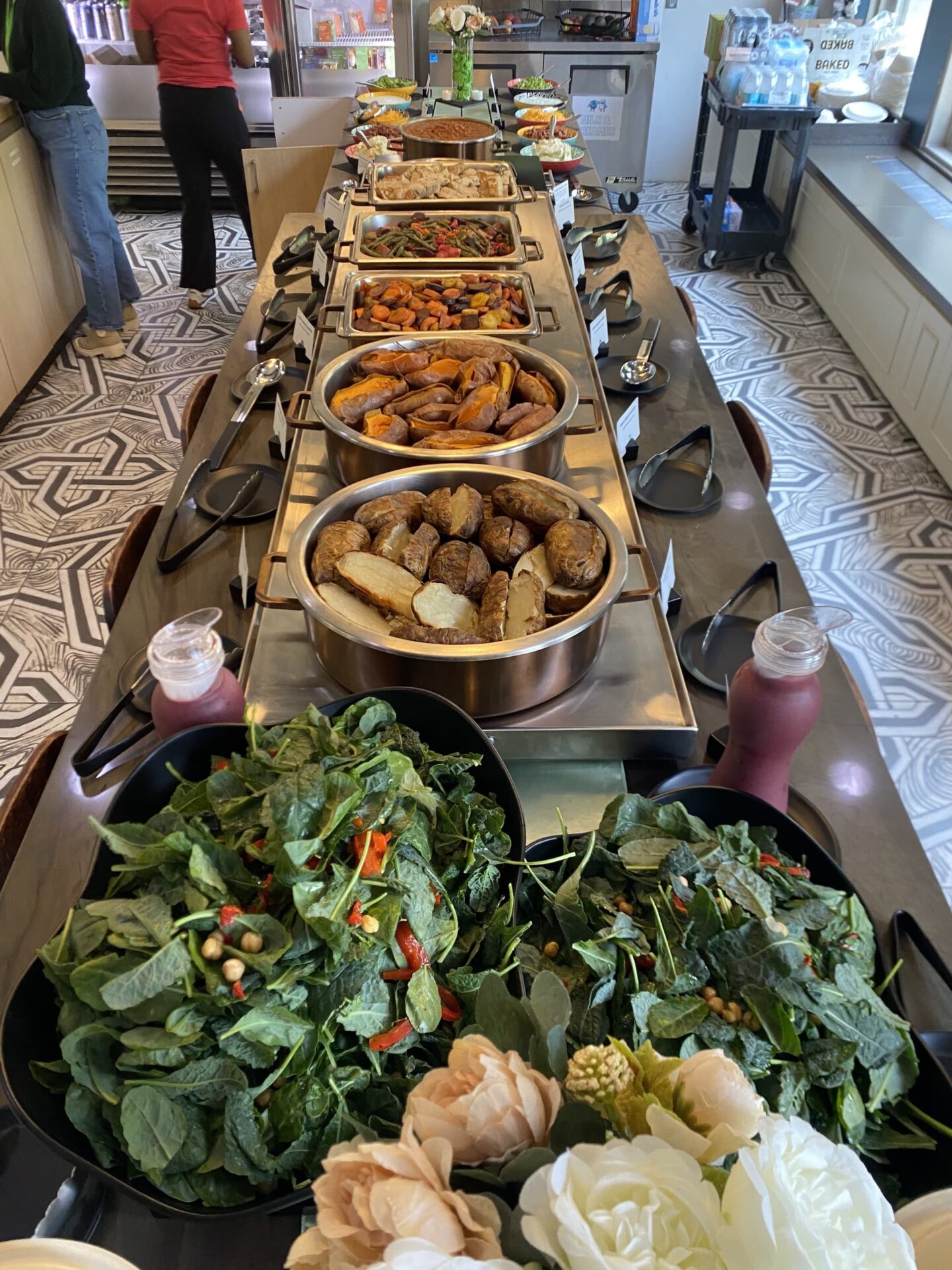 A long buffet table displays various dishes, including salads, roasted vegetables, prepared for corporate catering.