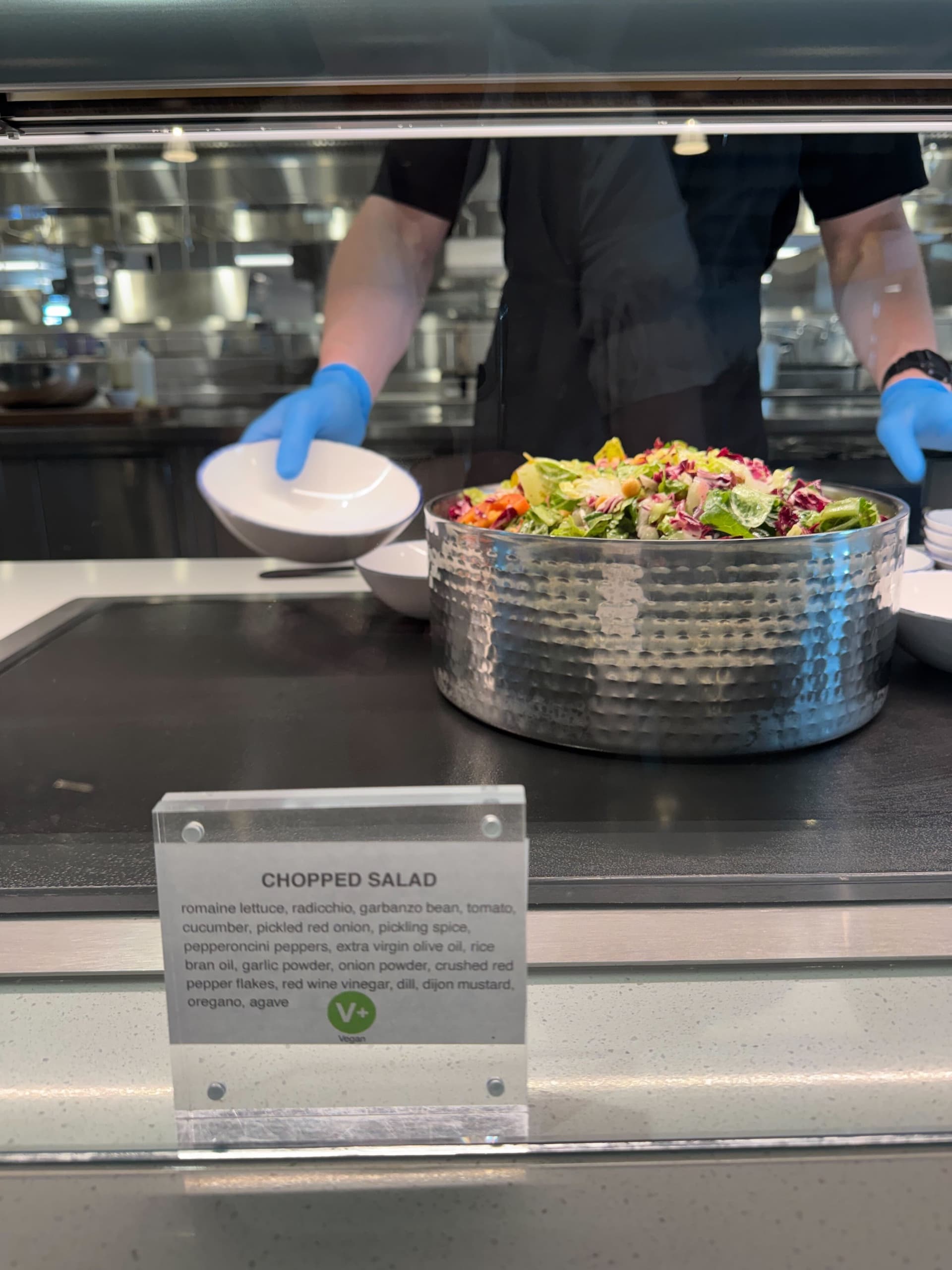 A chef serves a chopped salad from a metal bowl, with a sign detailing the ingredients.