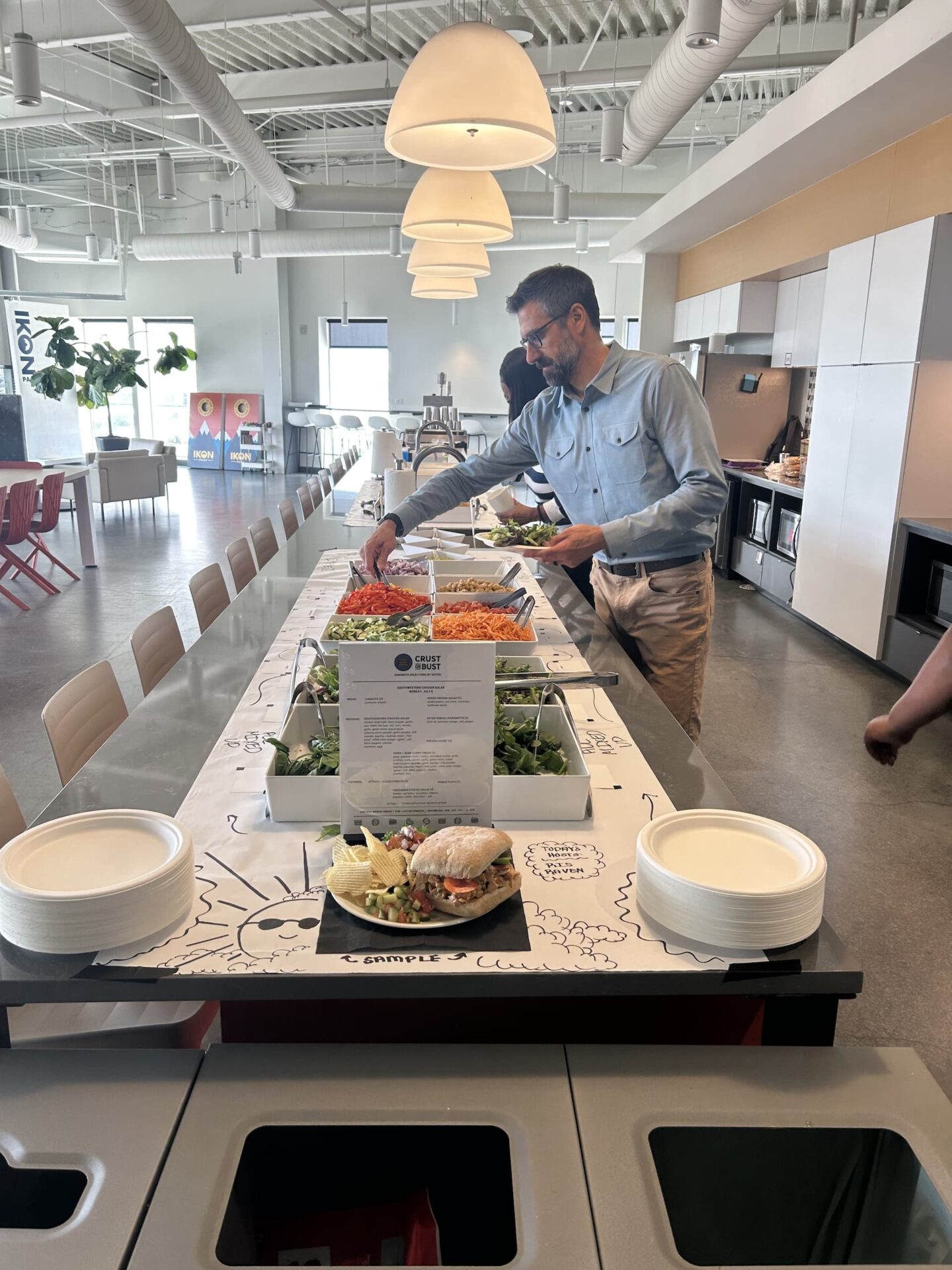 Corporate catering buffet setup with an array of fresh salad toppings and a custom sandwich display.